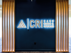 A neon CRI logo is set between Natural Casella Oak slatted detailing, combining brand identity with a natural design element that enhances the office’s welcoming atmosphere.