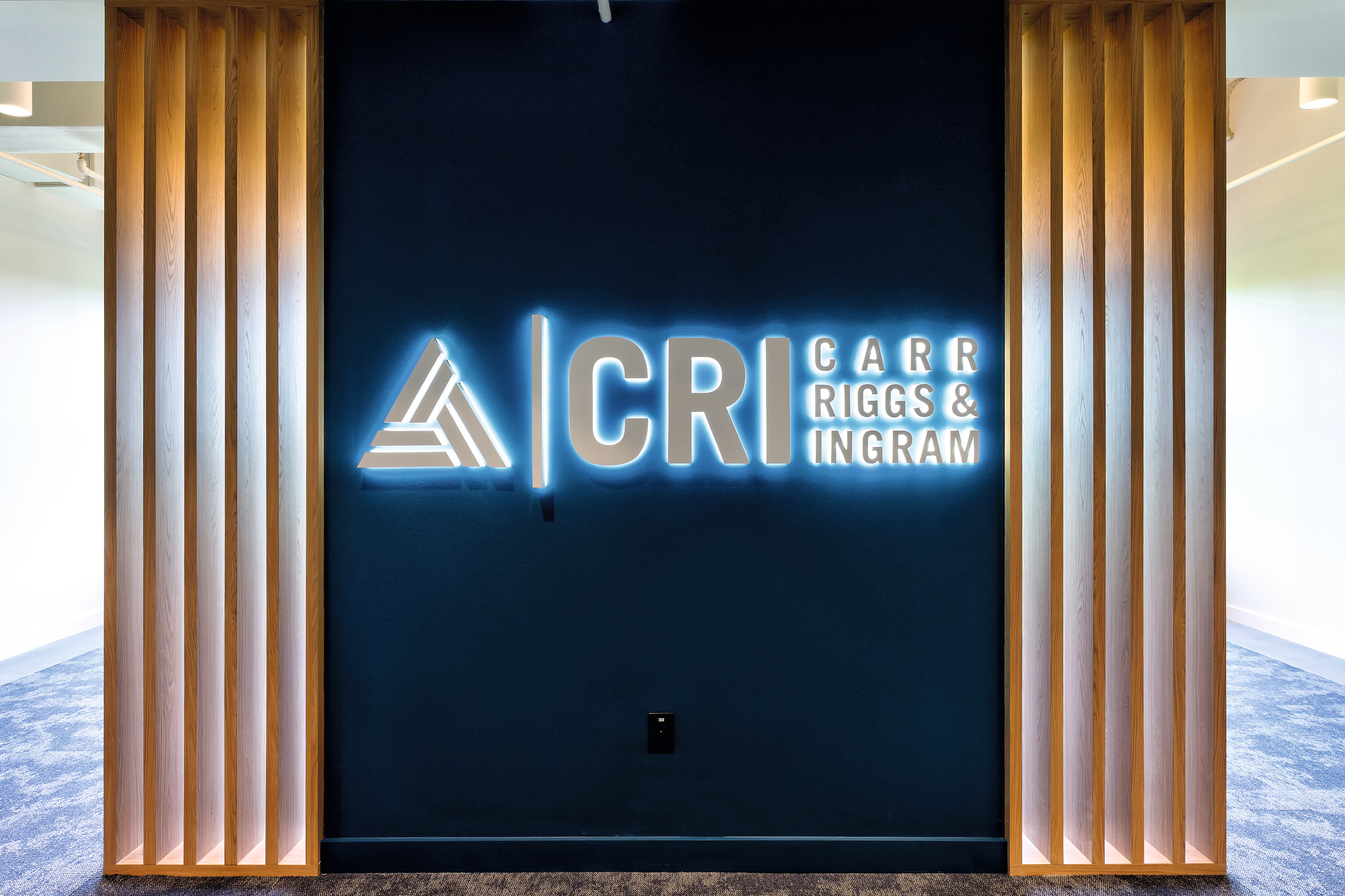 A neon CRI logo is set between Natural Casella Oak slatted detailing, combining brand identity with a natural design element that enhances the office’s welcoming atmosphere.