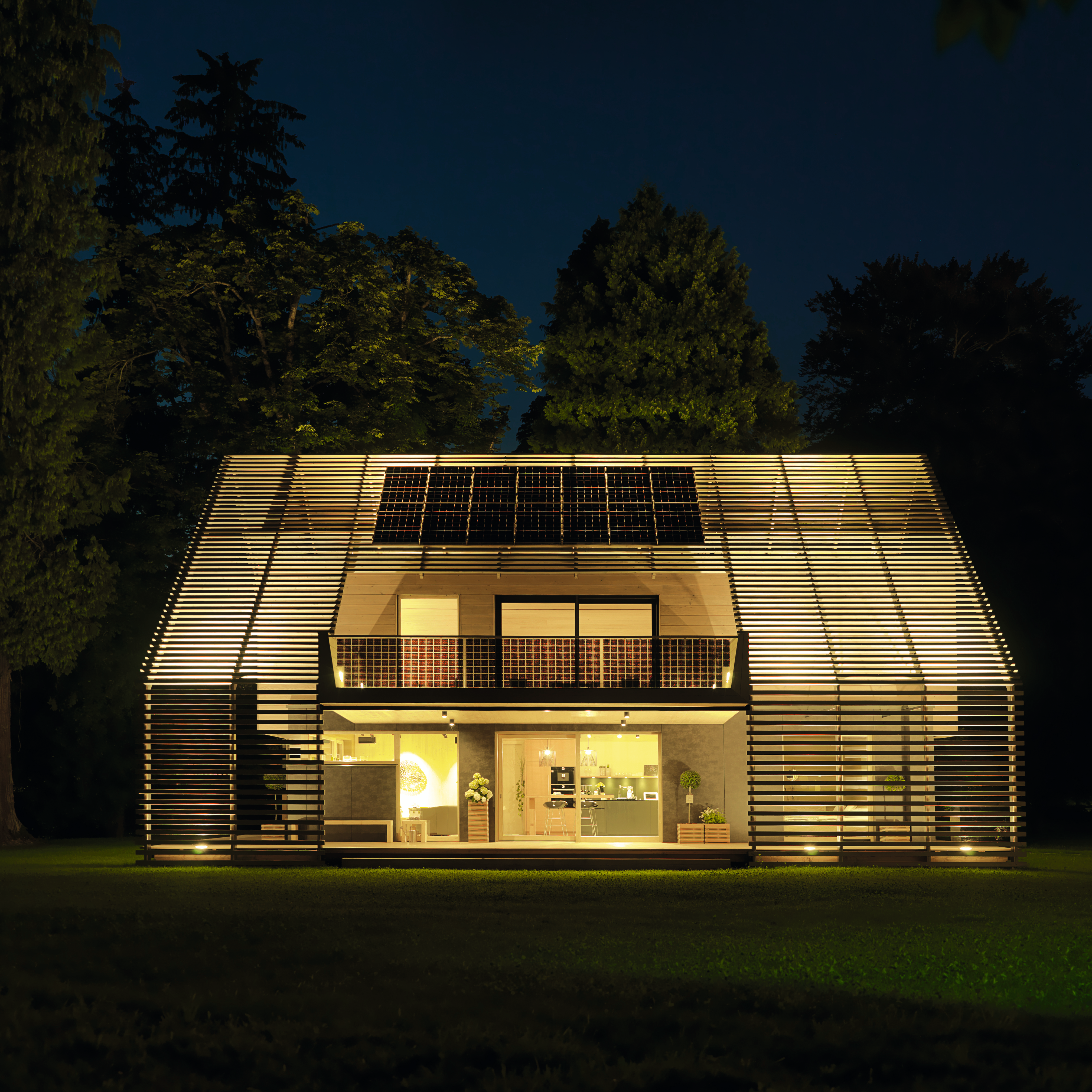 Modernes Passivhaus mit Holzfassade, großen Fenstern und Solarzellen bei Nacht 