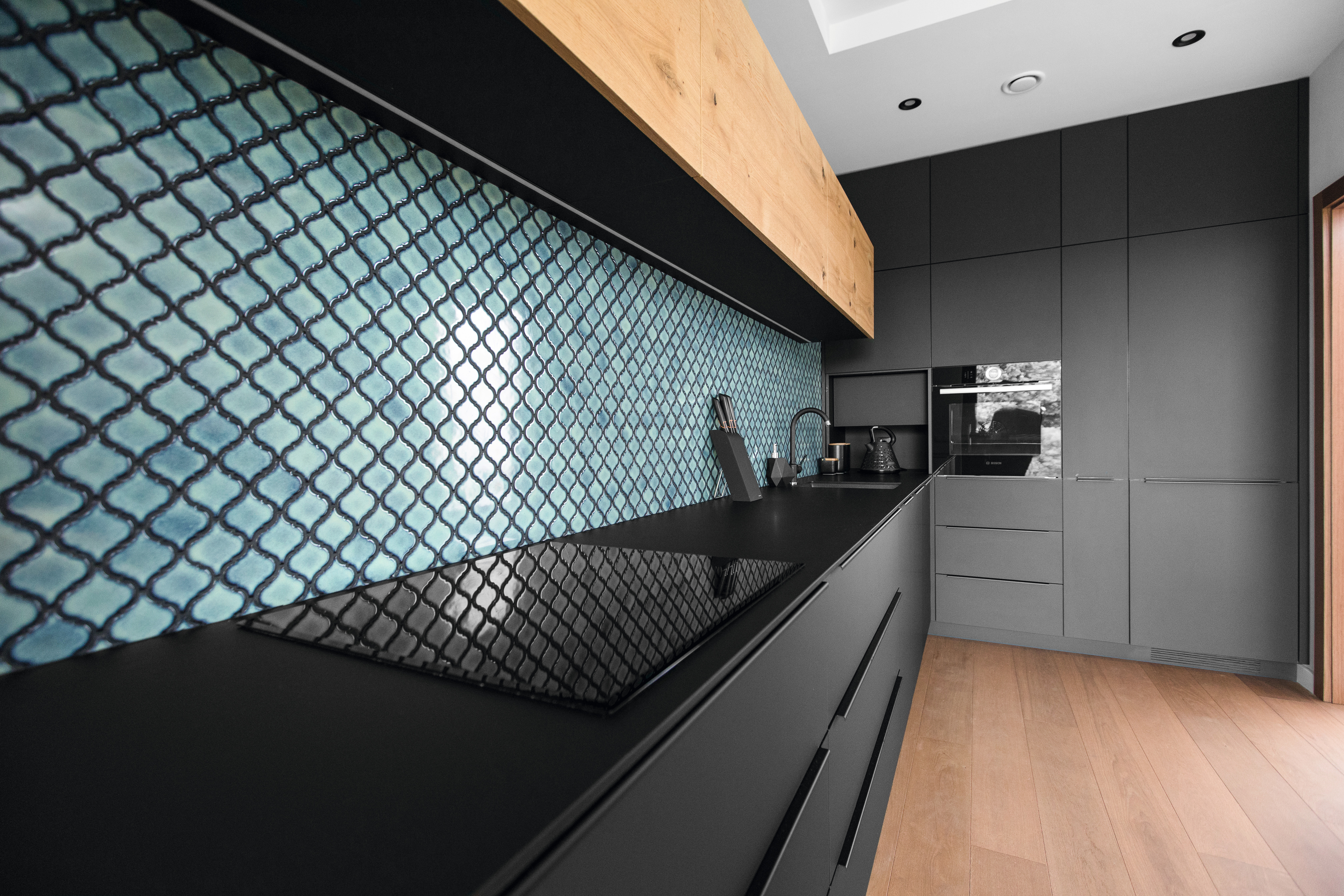 The black surface contrasts with the bright turquoise and mosaic design of the backsplash.