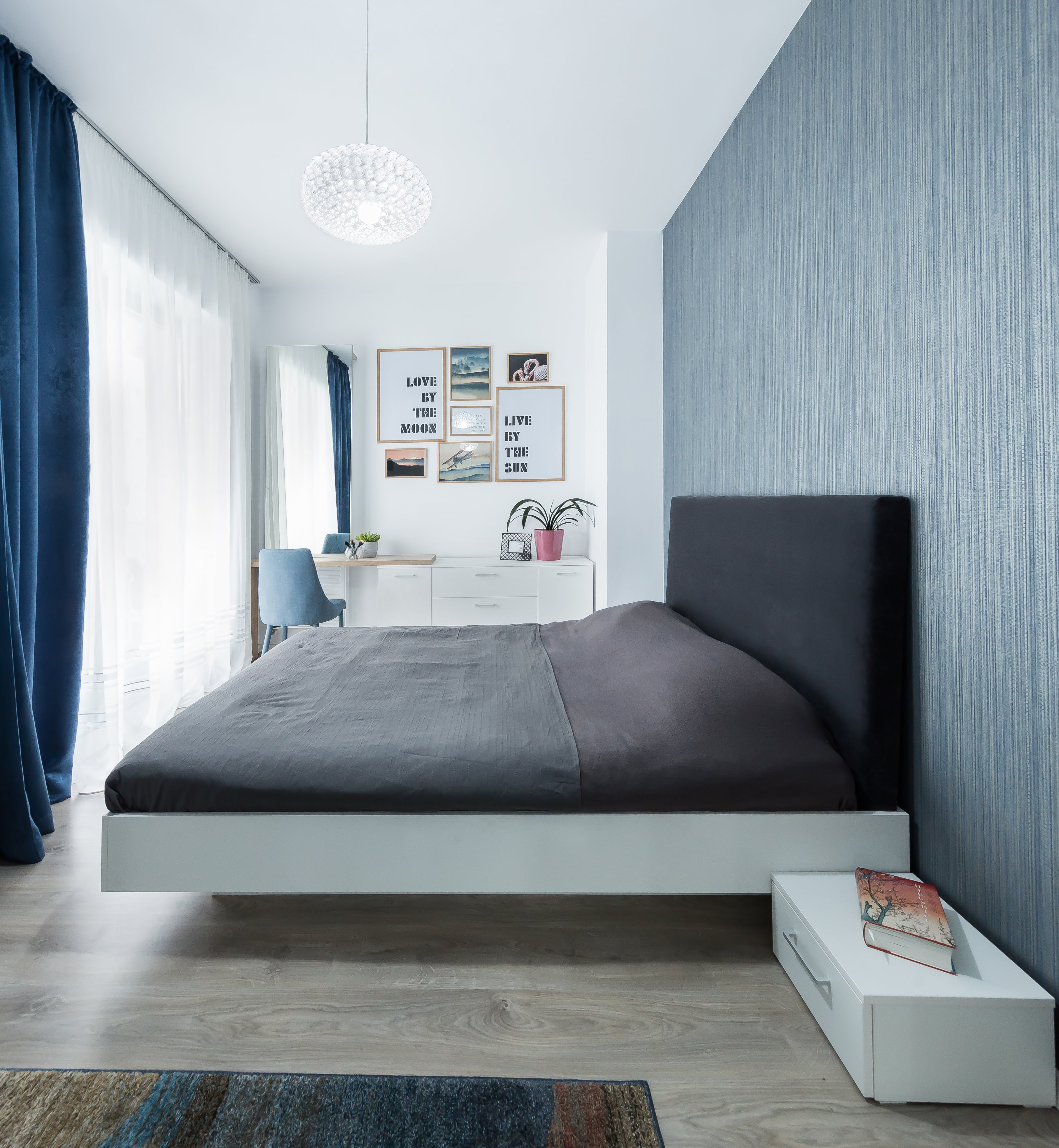 De subtiele blauwtint in de slaapkamer heeft niet alleen een kalmerend effect, maar fungeert ook als lichtschaduw. Het bed is groot in omvang, maar ziet er toch stijlvol en tijdloos uit dankzij het robuuste donkergrijze frame.