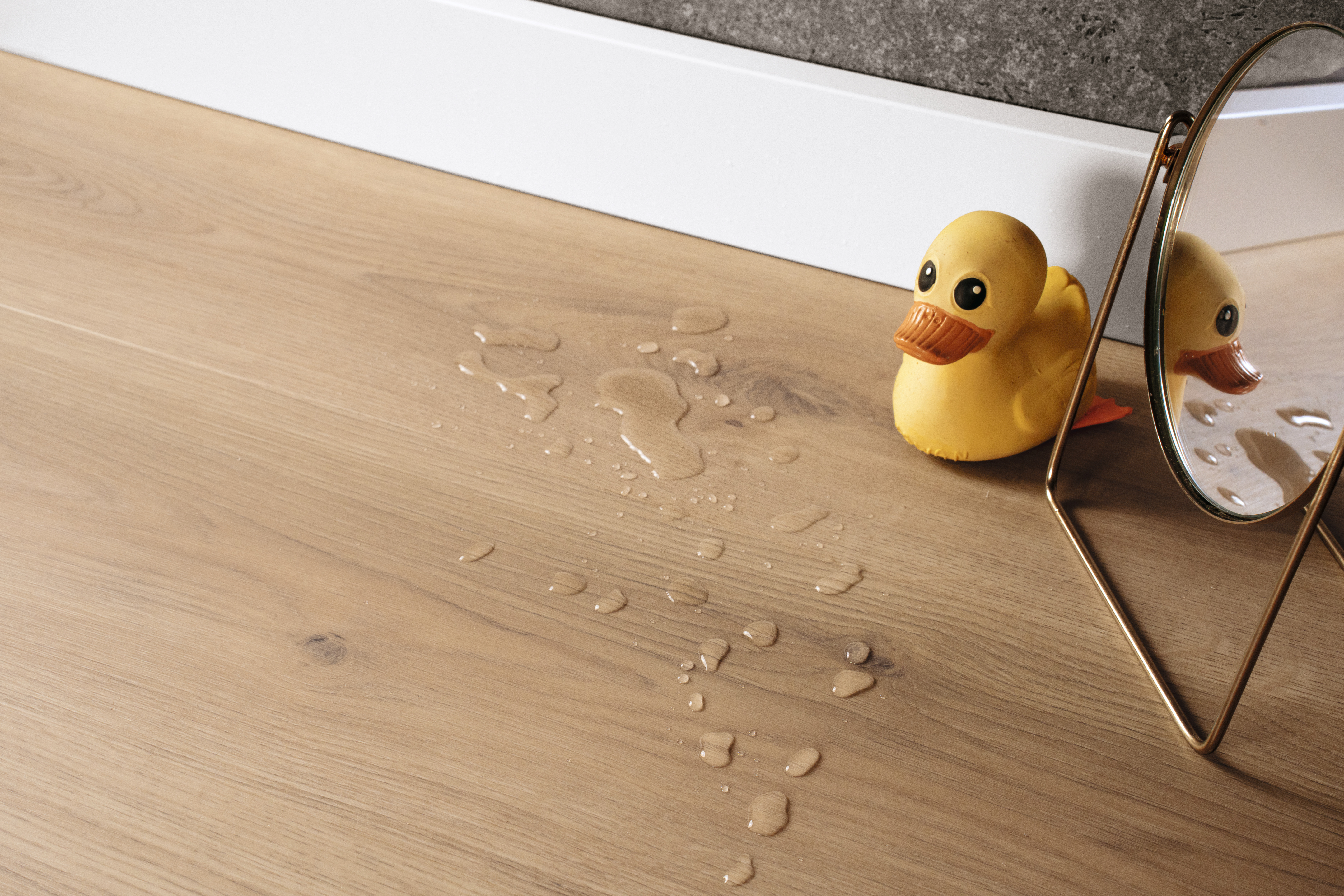 AquaDura+ Natural Messina Oak flooring with a rubber duck and water splashes – waterproof flooring in a natural oak look.