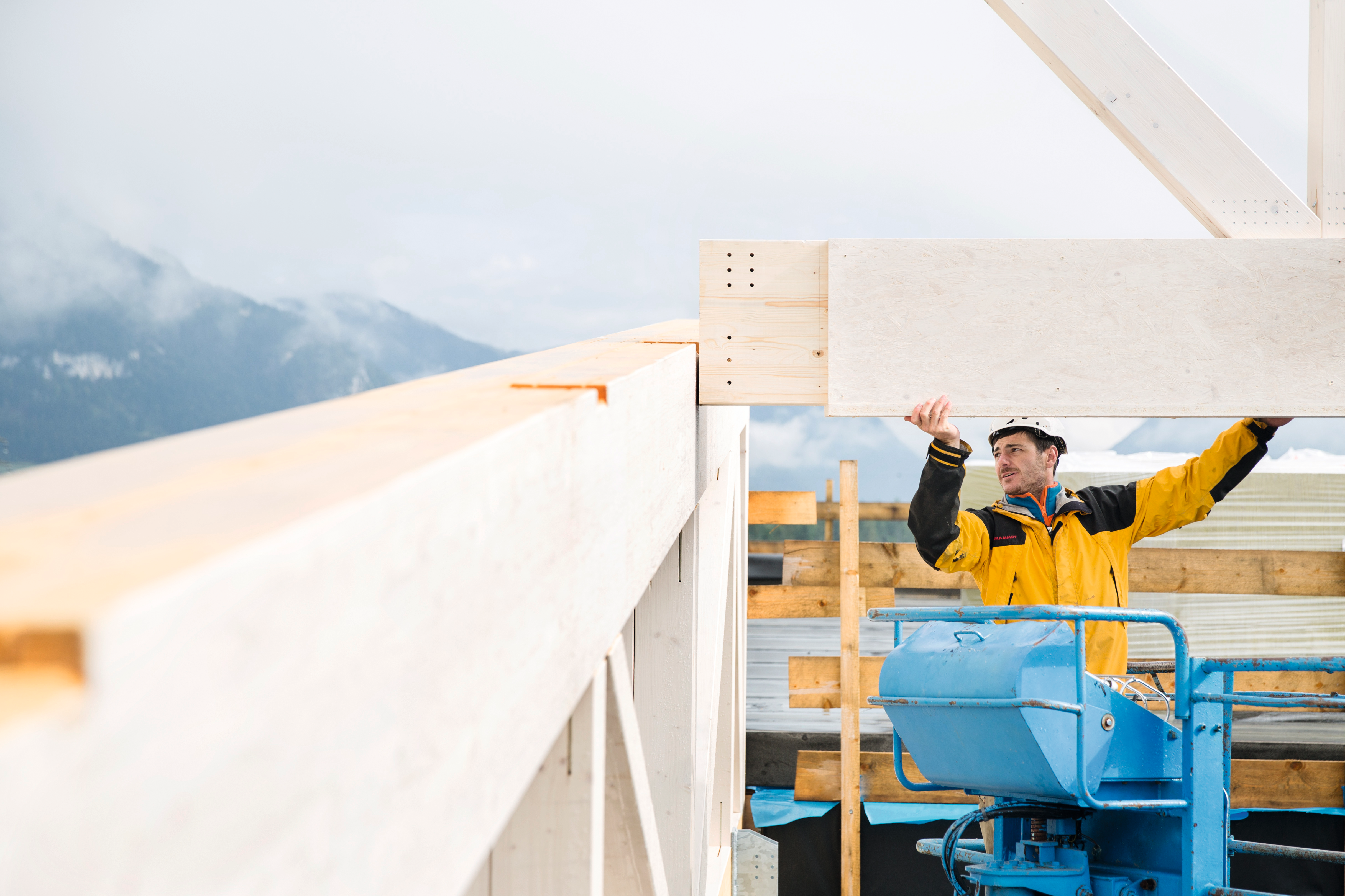Bauarbeiter beim Montieren eines Massivholzelements auf einer Baustelle in den Bergen.