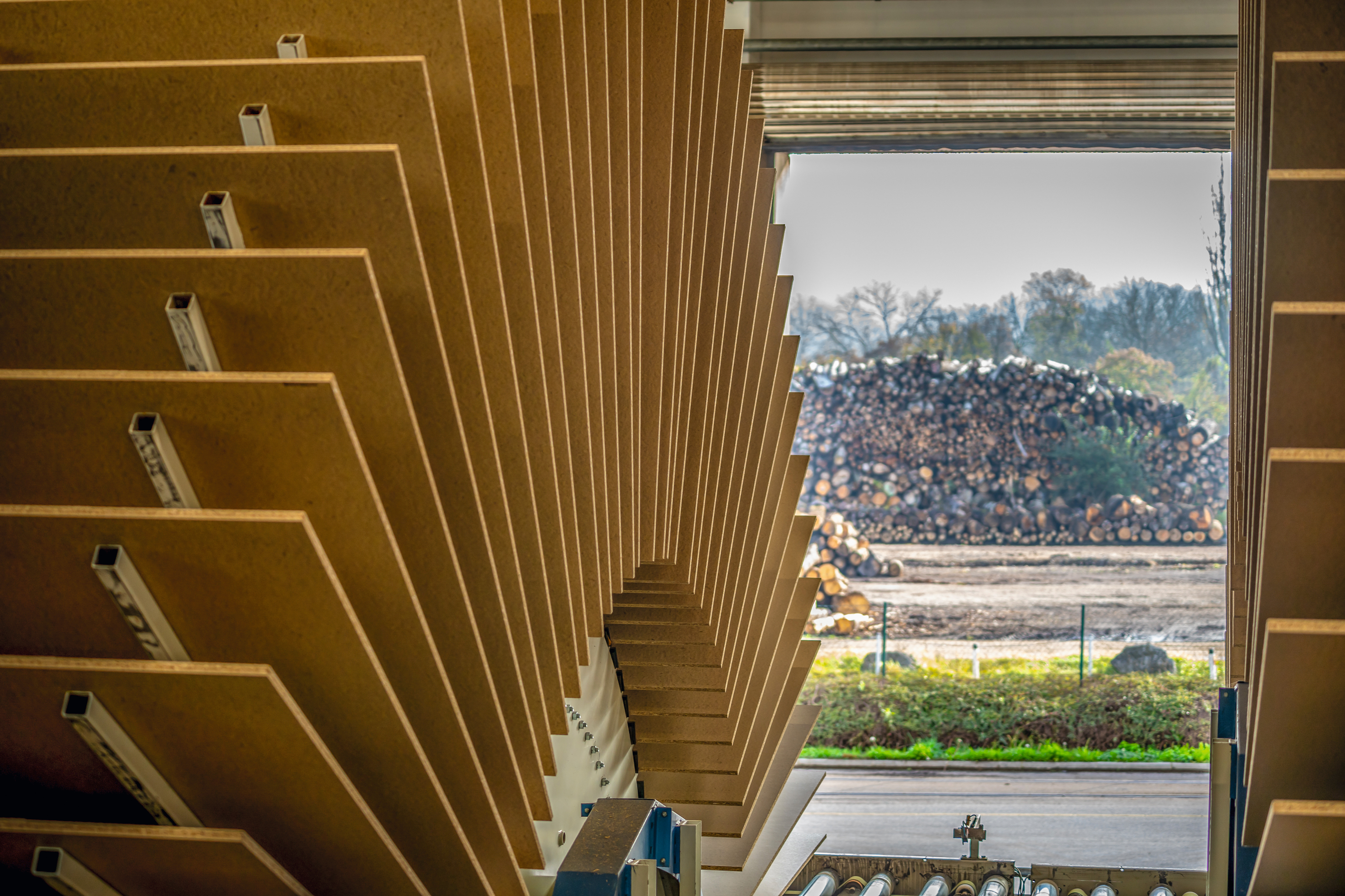 Chipboard turner in a hall with a view to the outside on the log yard with logs