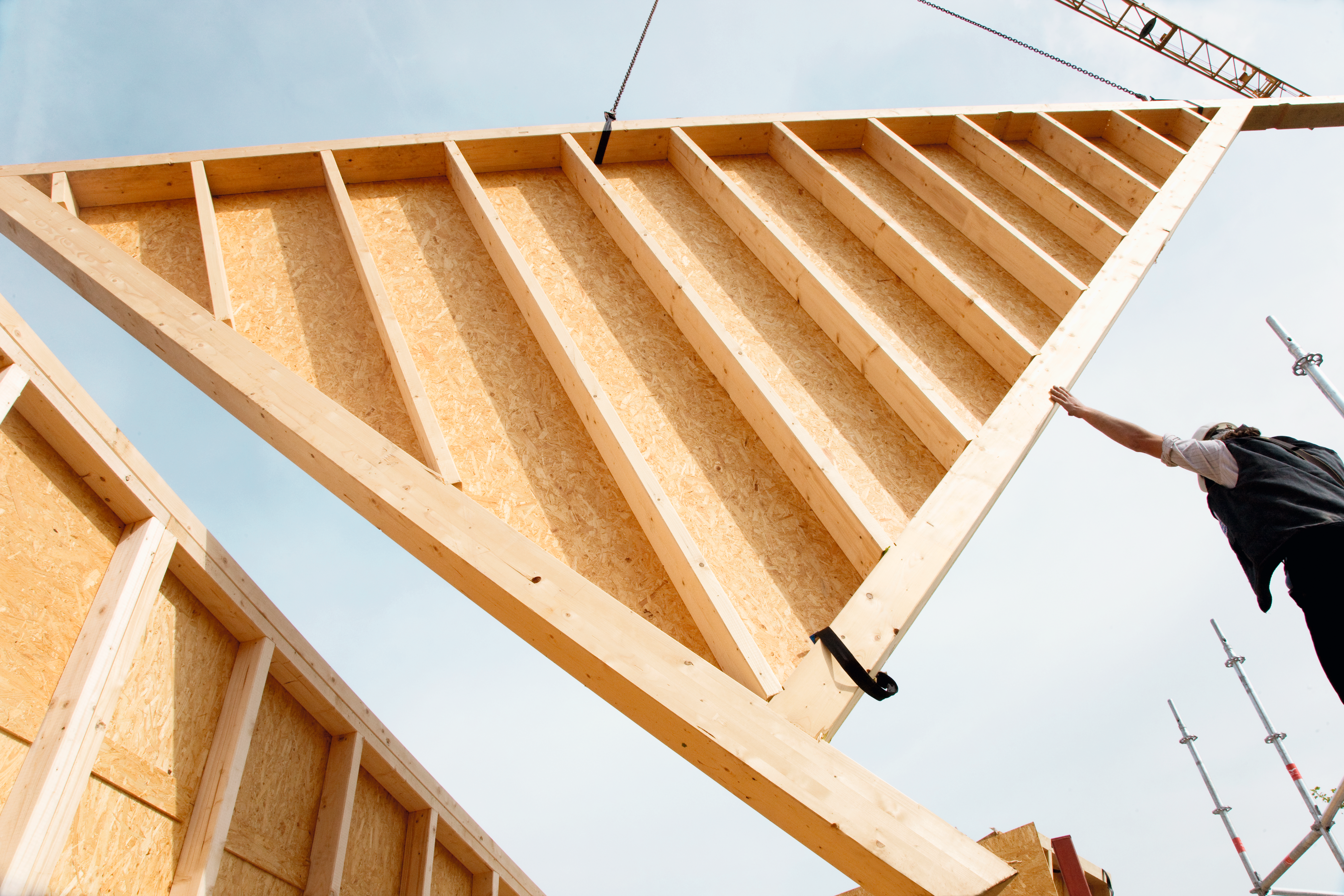 Montage eines Holzrahmenelements mit Kran auf einer Baustelle. 